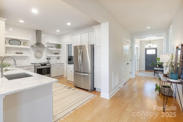 kitchen featuring sink, wall chimney range hood, appliances with stainless steel finishes, white cabinetry, and light stone counters