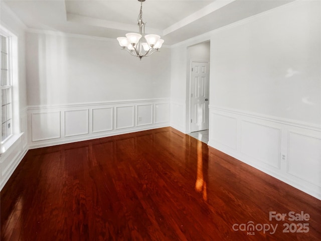 spare room with a tray ceiling, wood-type flooring, and a chandelier