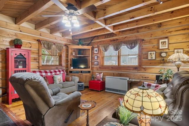 living room featuring beamed ceiling, ceiling fan, light wood-type flooring, and wooden walls