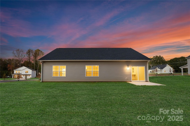 back house at dusk featuring a patio area and a lawn