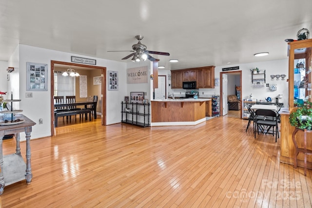 living room with ceiling fan with notable chandelier and light hardwood / wood-style floors