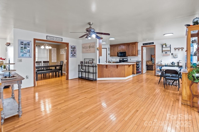 living room with sink, ceiling fan with notable chandelier, and light hardwood / wood-style floors