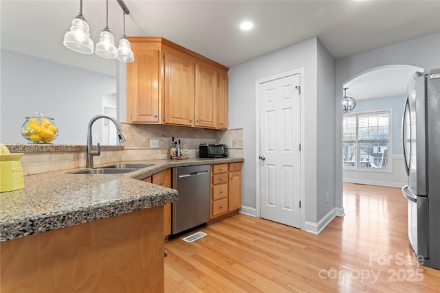 kitchen with decorative light fixtures, sink, backsplash, stainless steel appliances, and light hardwood / wood-style flooring