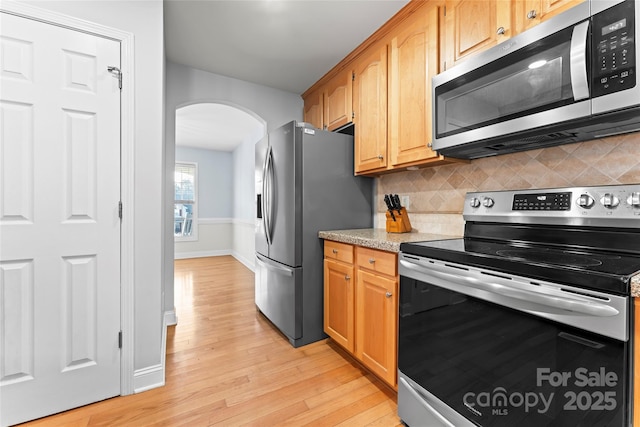 kitchen with tasteful backsplash, light stone counters, light hardwood / wood-style flooring, and appliances with stainless steel finishes