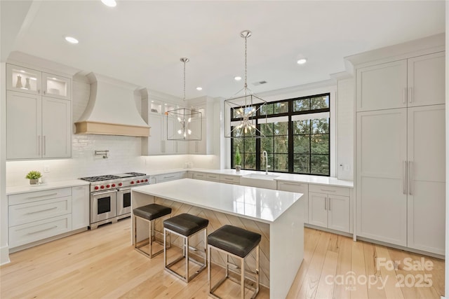 kitchen featuring range with two ovens, light wood-style flooring, custom exhaust hood, light countertops, and a sink