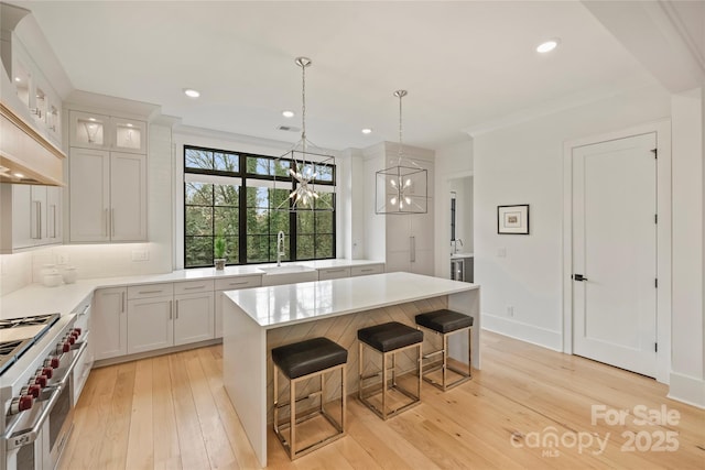 kitchen with a sink, light countertops, double oven range, light wood-type flooring, and a center island