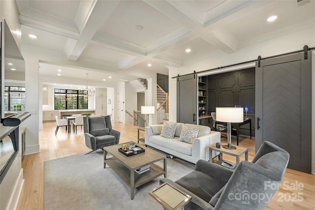 living area with beam ceiling, coffered ceiling, light wood-style flooring, and a barn door