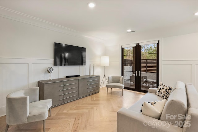 living area featuring a decorative wall, visible vents, french doors, wainscoting, and crown molding