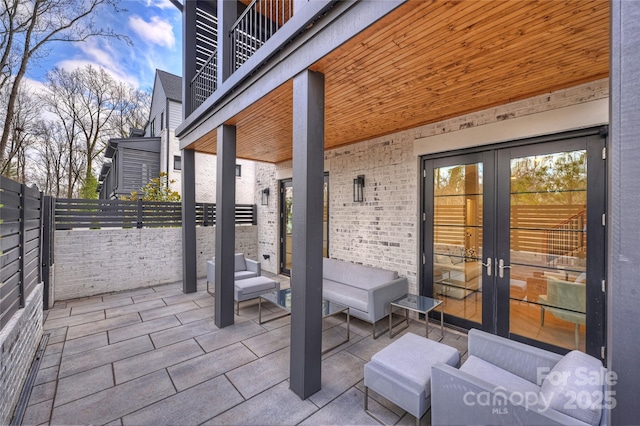 view of patio featuring french doors, fence, and a balcony