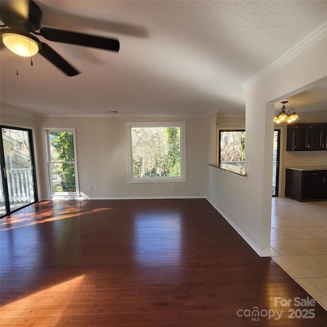 spare room with wood-type flooring, ornamental molding, ceiling fan with notable chandelier, and a textured ceiling