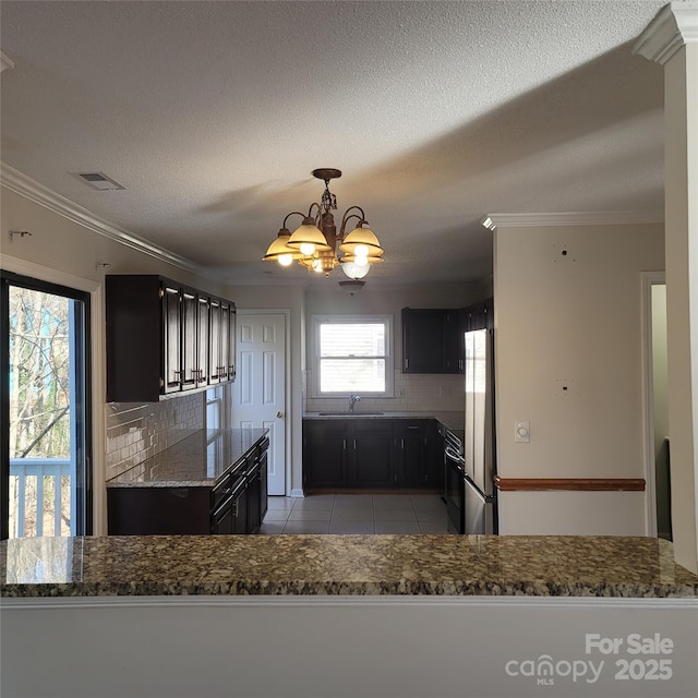 kitchen featuring tasteful backsplash, dark stone countertops, ornamental molding, fridge, and light tile patterned floors