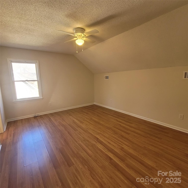 additional living space featuring lofted ceiling, a textured ceiling, dark wood-type flooring, and ceiling fan