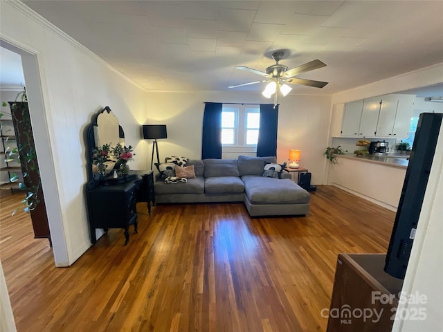 living area with crown molding, a ceiling fan, and wood finished floors