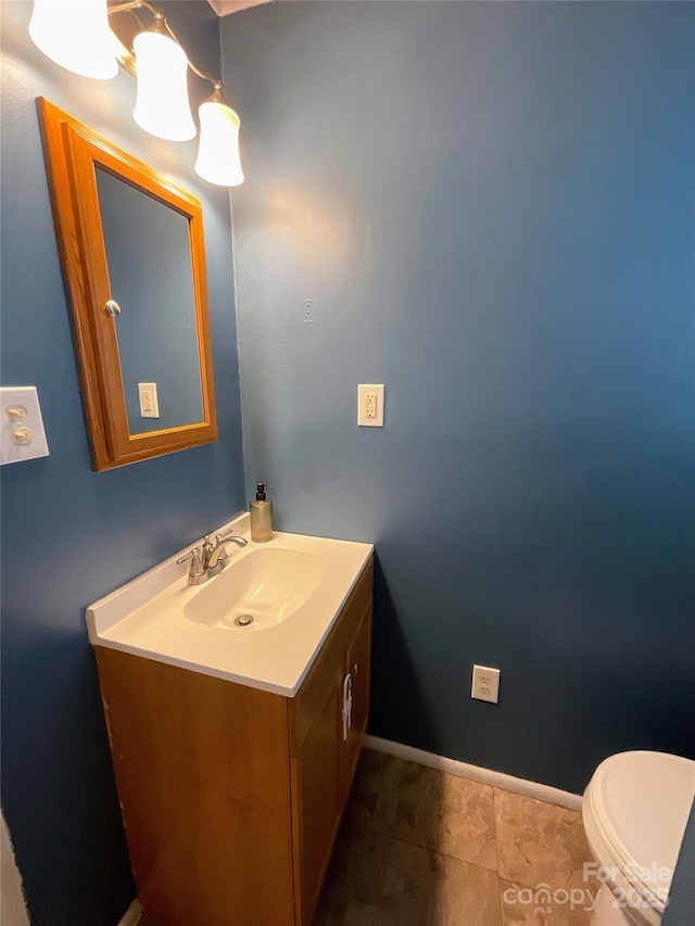 half bath with toilet, baseboards, and vanity