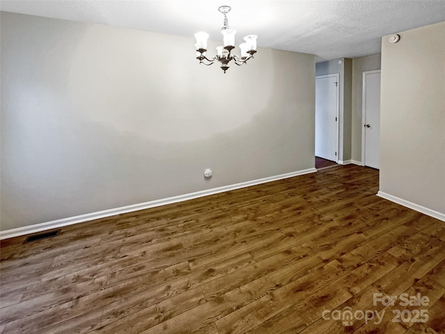 empty room with dark hardwood / wood-style flooring, a chandelier, and a textured ceiling