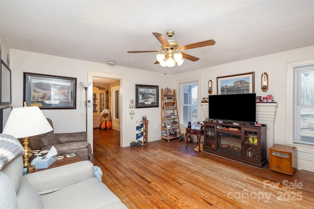 living room featuring hardwood / wood-style flooring, ceiling fan, and a textured ceiling