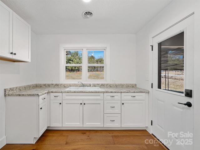 kitchen featuring white cabinetry, light hardwood / wood-style floors, sink, and a wealth of natural light