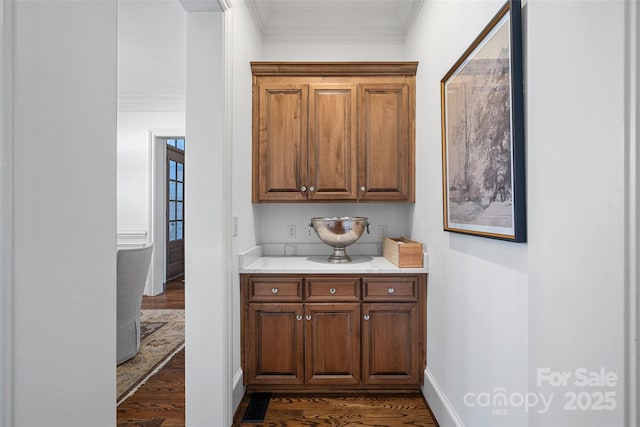 bar featuring light stone counters, ornamental molding, and dark hardwood / wood-style flooring