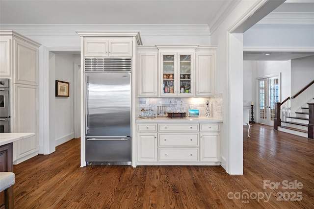 kitchen featuring appliances with stainless steel finishes, white cabinetry, backsplash, ornamental molding, and dark wood-type flooring