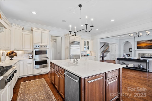 kitchen with sink, hanging light fixtures, stainless steel appliances, light stone countertops, and a center island with sink