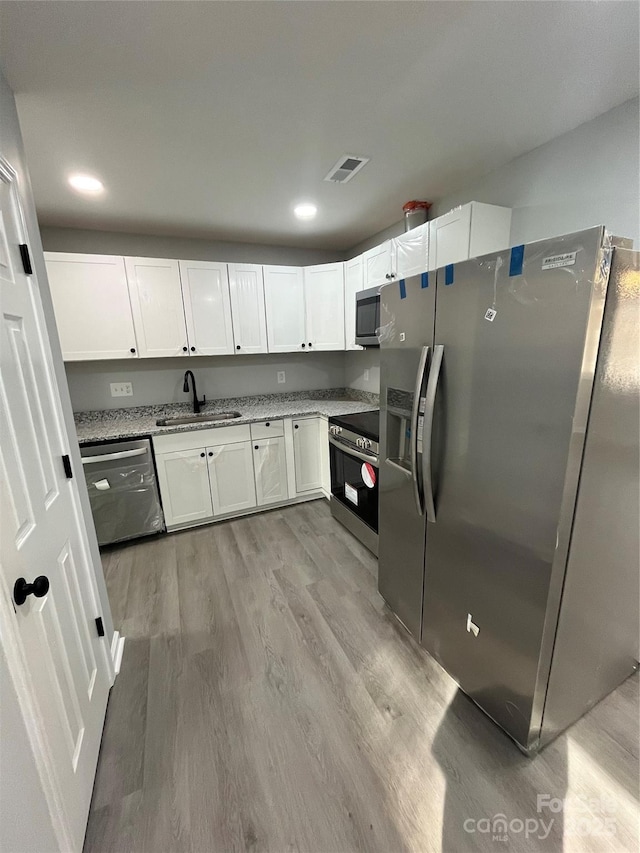 kitchen featuring sink, white cabinetry, stainless steel appliances, light stone countertops, and light wood-type flooring