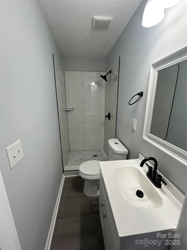 bathroom featuring a tile shower, vanity, and toilet