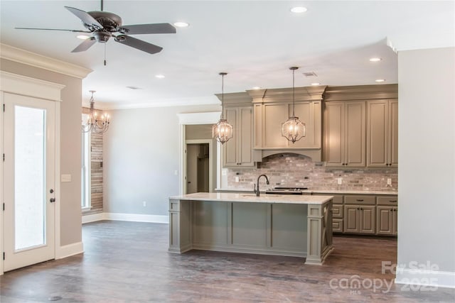 kitchen with an island with sink, ornamental molding, pendant lighting, and backsplash