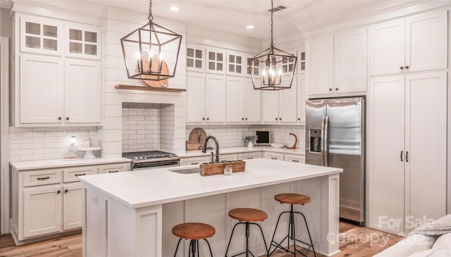 kitchen featuring sink, white cabinets, stainless steel fridge, stove, and a kitchen island with sink