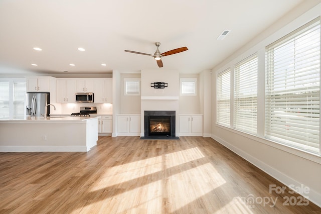 unfurnished living room with sink, light hardwood / wood-style floors, and ceiling fan