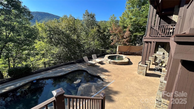 view of patio / terrace featuring an outdoor hot tub, fence, a balcony, a mountain view, and an outdoor pool