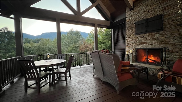 sunroom / solarium featuring lofted ceiling with beams, an outdoor stone fireplace, and a mountain view