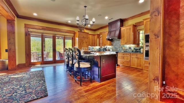 kitchen featuring crown molding, light wood finished floors, decorative backsplash, an inviting chandelier, and stainless steel oven