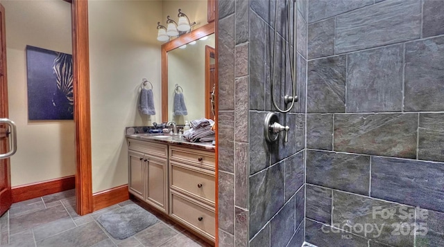 bathroom featuring tiled shower, vanity, and baseboards