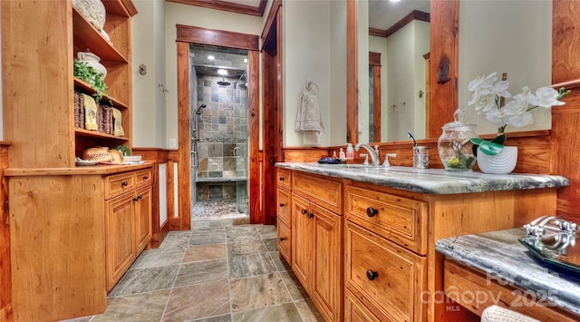 full bath with crown molding, stone finish flooring, wainscoting, a shower stall, and vanity