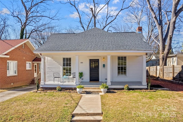 bungalow-style home featuring a chimney, roof with shingles, covered porch, fence, and a front yard