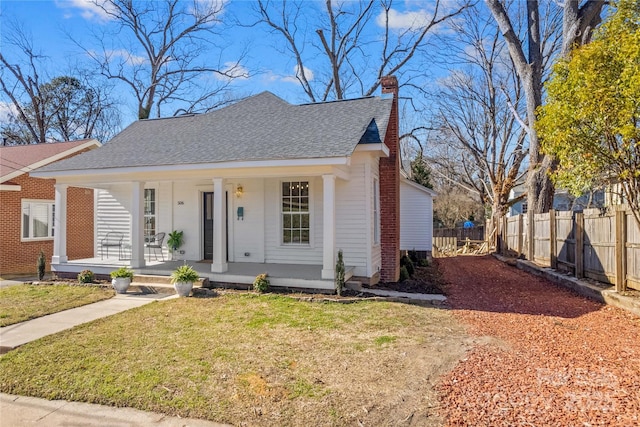 bungalow-style house featuring covered porch, fence, roof with shingles, a chimney, and a front yard