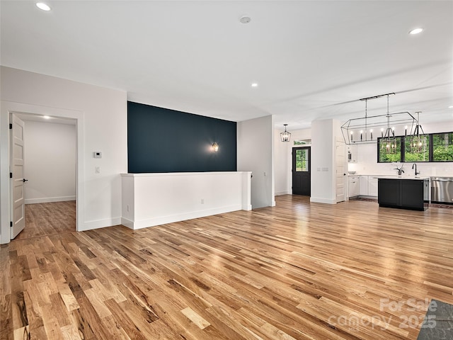 unfurnished living room featuring an inviting chandelier and light hardwood / wood-style floors