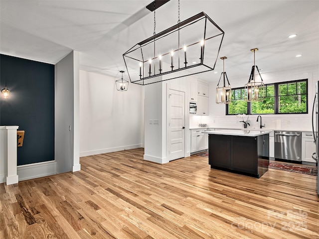 kitchen with white cabinetry, a center island, stainless steel dishwasher, pendant lighting, and light hardwood / wood-style floors