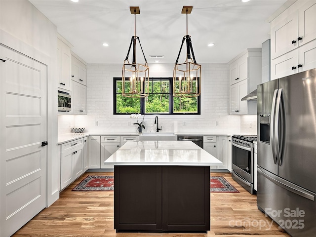 kitchen featuring stainless steel appliances, white cabinetry, a kitchen island, and sink