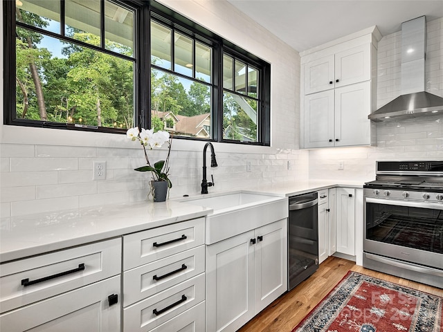 kitchen with wall chimney exhaust hood, stainless steel range oven, sink, and white cabinets