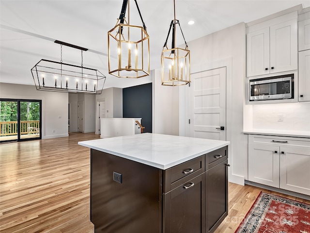 kitchen featuring pendant lighting, dark brown cabinets, stainless steel microwave, tasteful backsplash, and white cabinets