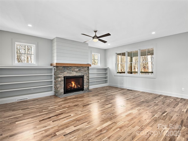 unfurnished living room featuring ceiling fan, a stone fireplace, and light hardwood / wood-style floors