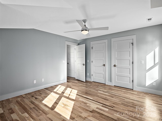 unfurnished bedroom featuring multiple closets, light hardwood / wood-style flooring, ceiling fan, and vaulted ceiling