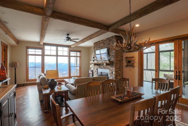 dining room featuring beamed ceiling, ceiling fan, a stone fireplace, and dark hardwood / wood-style flooring