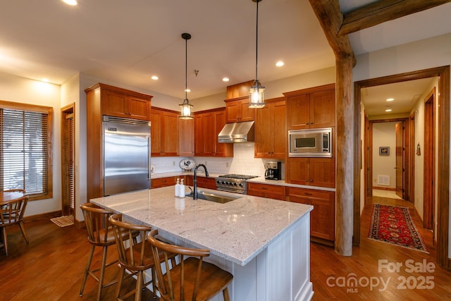 kitchen featuring a breakfast bar, sink, a kitchen island with sink, built in appliances, and light stone counters