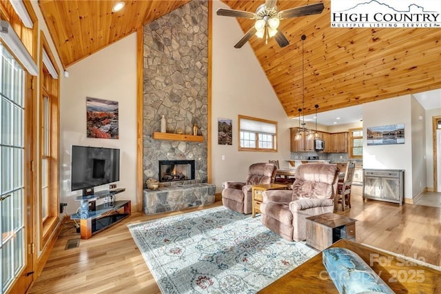 living room with wood ceiling, ceiling fan, a stone fireplace, and light hardwood / wood-style floors