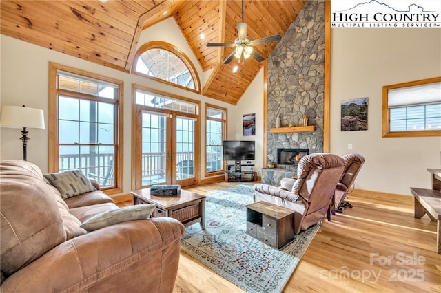 living room featuring french doors, a stone fireplace, wood ceiling, high vaulted ceiling, and light hardwood / wood-style flooring