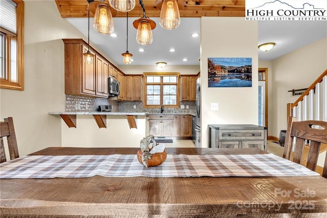 kitchen featuring a breakfast bar area, decorative light fixtures, kitchen peninsula, stainless steel appliances, and light stone countertops