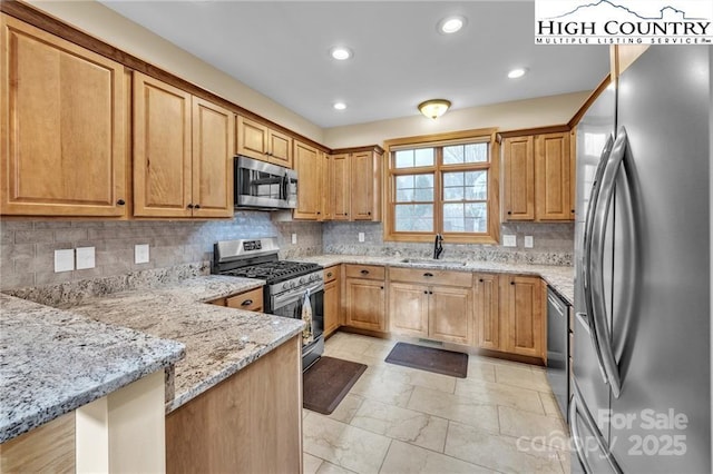 kitchen with sink, appliances with stainless steel finishes, light stone counters, decorative backsplash, and kitchen peninsula