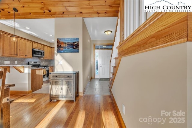 kitchen with a breakfast bar, light hardwood / wood-style flooring, pendant lighting, stainless steel appliances, and backsplash